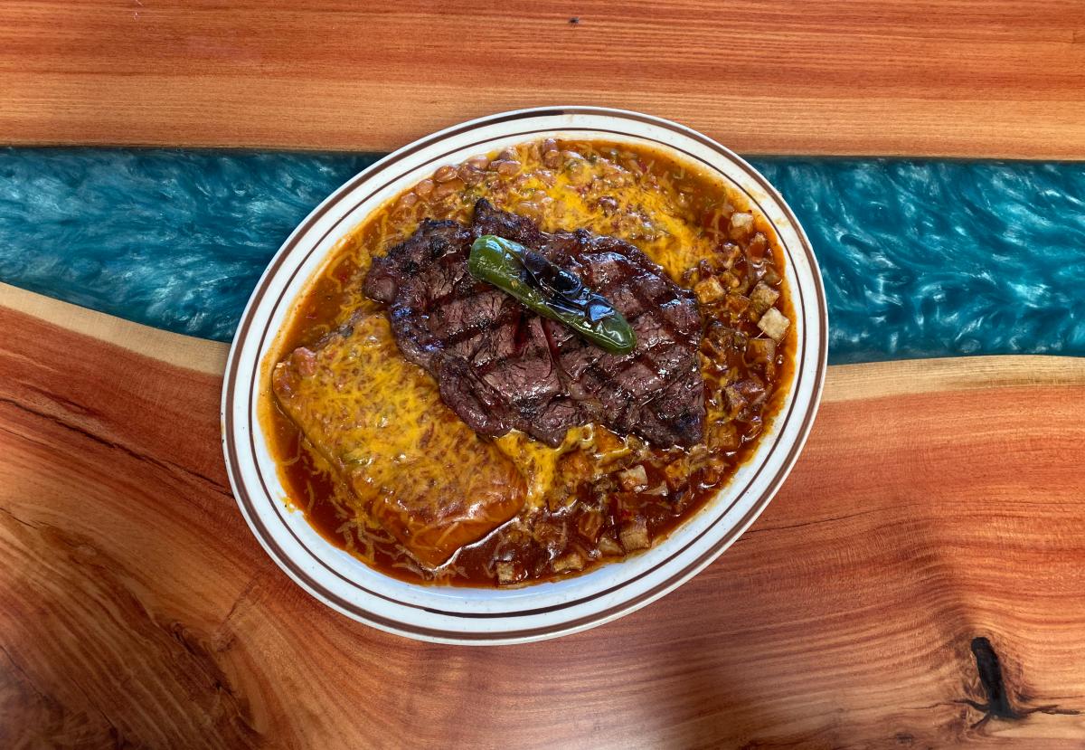 A plate of food from Sadie's featuring a ribeye, tamale, beans and potatoes smothered in red and green chile.