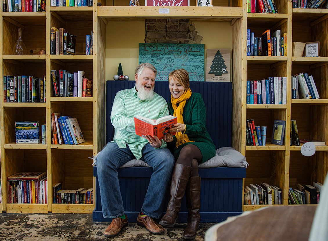 A man and a woman sit on a wooden bench surrounded by bookshelves at The Story Keeper Bookstore in Downtown Selma, NC.