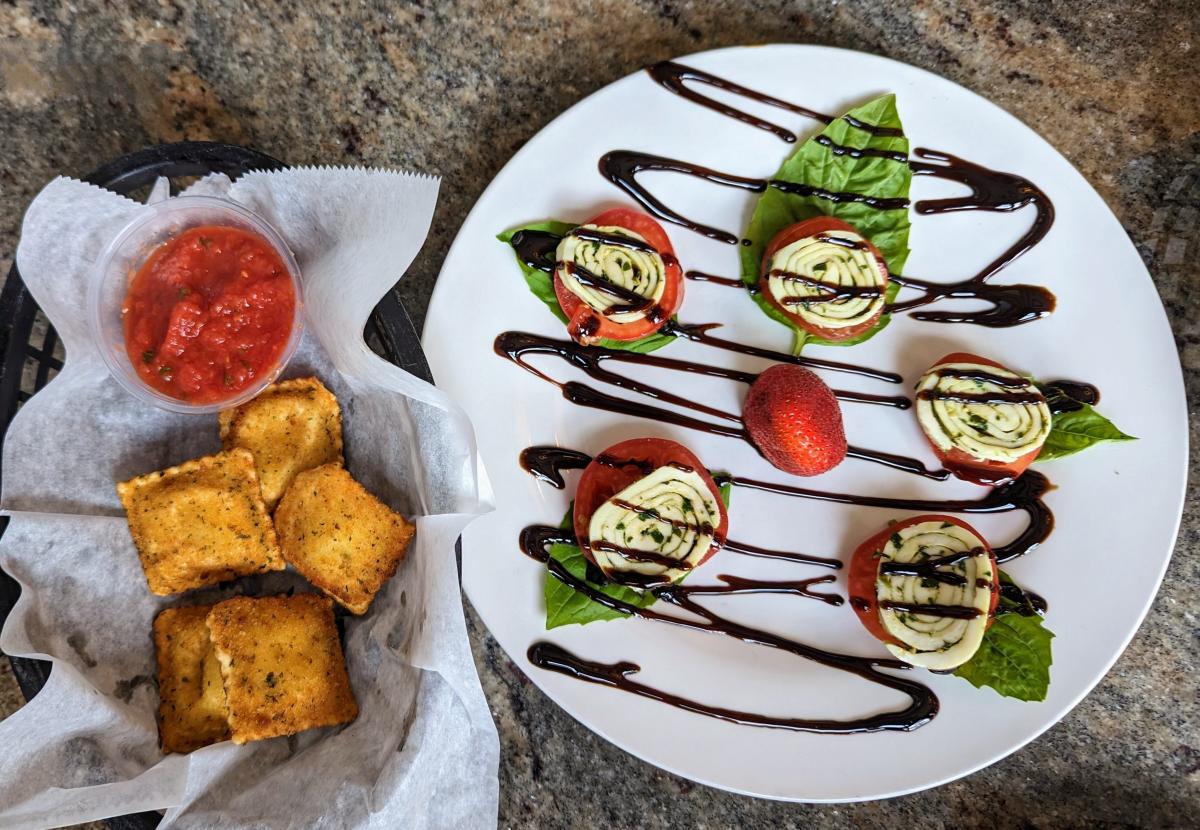 Image is of cheese ravioli bites with a cup of marina sauce and a plate that has tomato's with spirals of mozzarella cheese and a balsamic glaze.