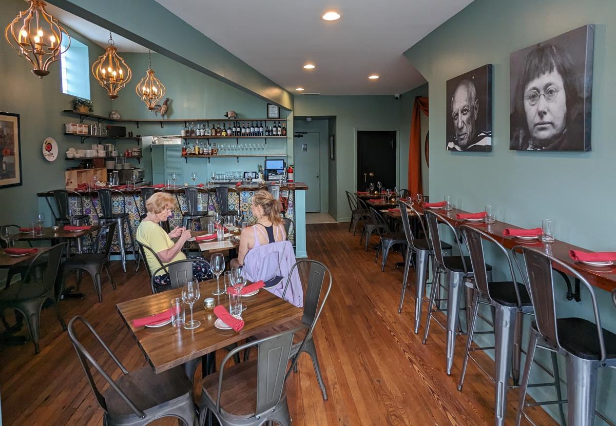 Image is looking inside the dining room with tables in the foreground, long table along the wall on the right with bar top chairs and a bar in the background.