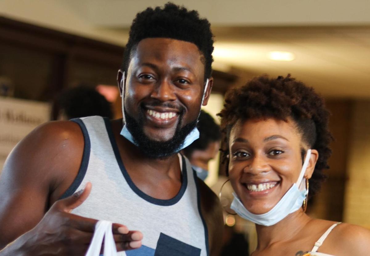 An African-American man and woman smiling at the camera. Their face covers are down around their chins.