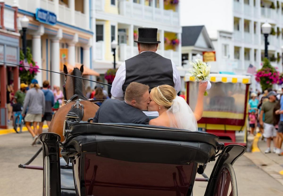 Bride and groom on horse-drawn carriage ride through downtown Mackinac Island after wedding