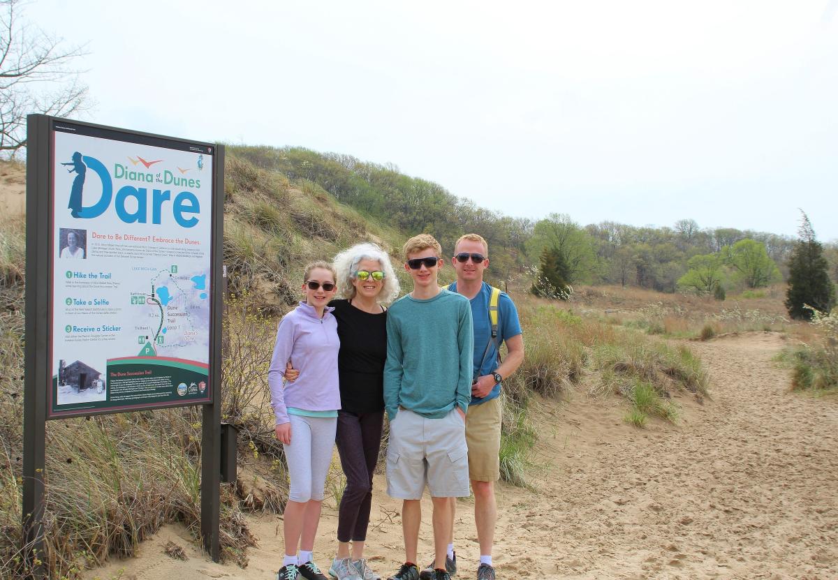 A group of four people stand on a sandy trail next to a sign.