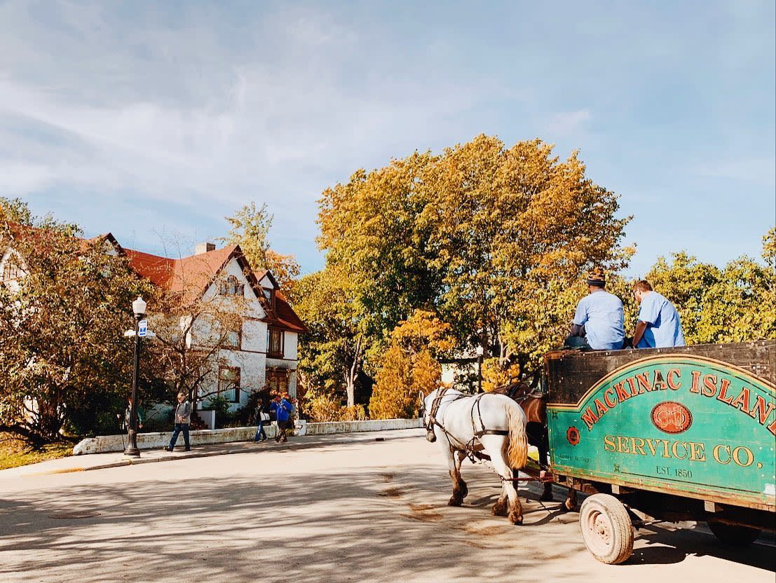 A Mackinac Island Service Co. dray is pulled by horses around a street corner on a sunny fall day