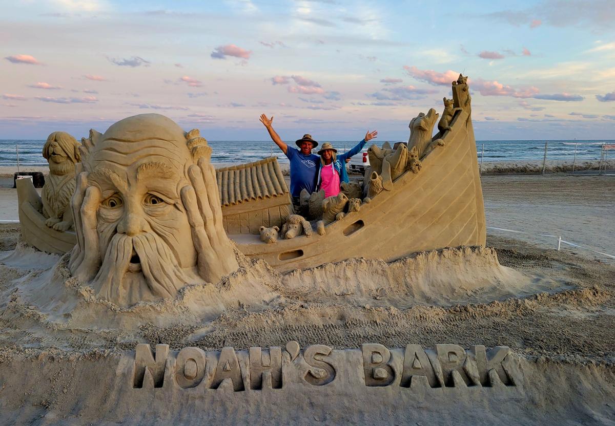 A large sand sculpture depicting an ark full of dogs and a large face looking worried.