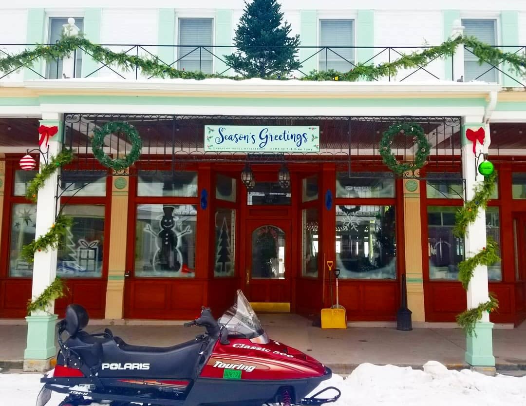 Snowmobile parked at Mackinac Island storefront decorated for Christmas with a tree on the roof