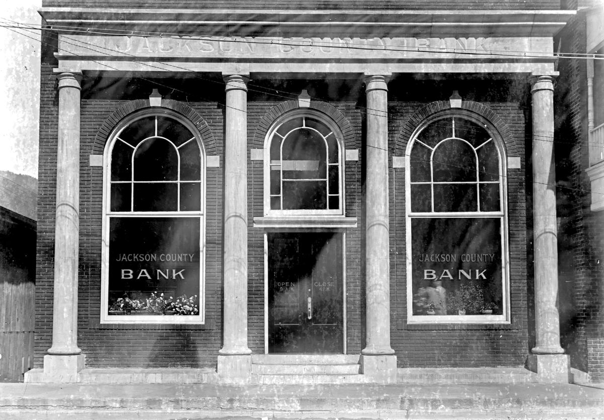 Columned brick front of the Jackson County Bank in Sylva, NC, with tall arched windows, potted flowers and posted 9 a.m. to 4 p.m. hours