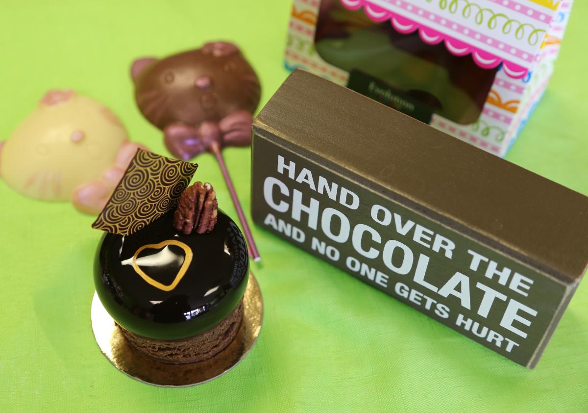 A chocolate dessert is topped with candy and a gold heart. A sign sits to the right that says "Hand over the chocolate and no one gets hurt." Other candy is blurred in the background