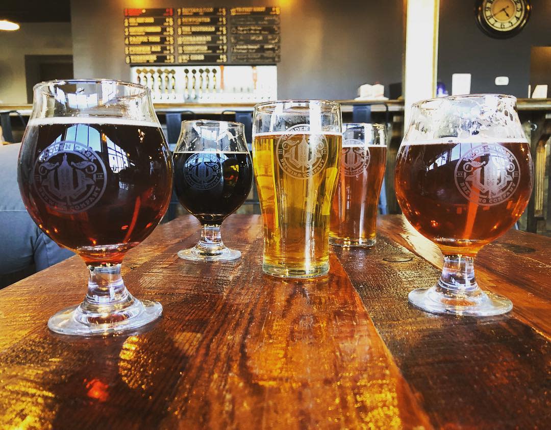 five glasses of different colored beer on a wooden table with a menu board in the background at wooden cask brewery in newport kentucky