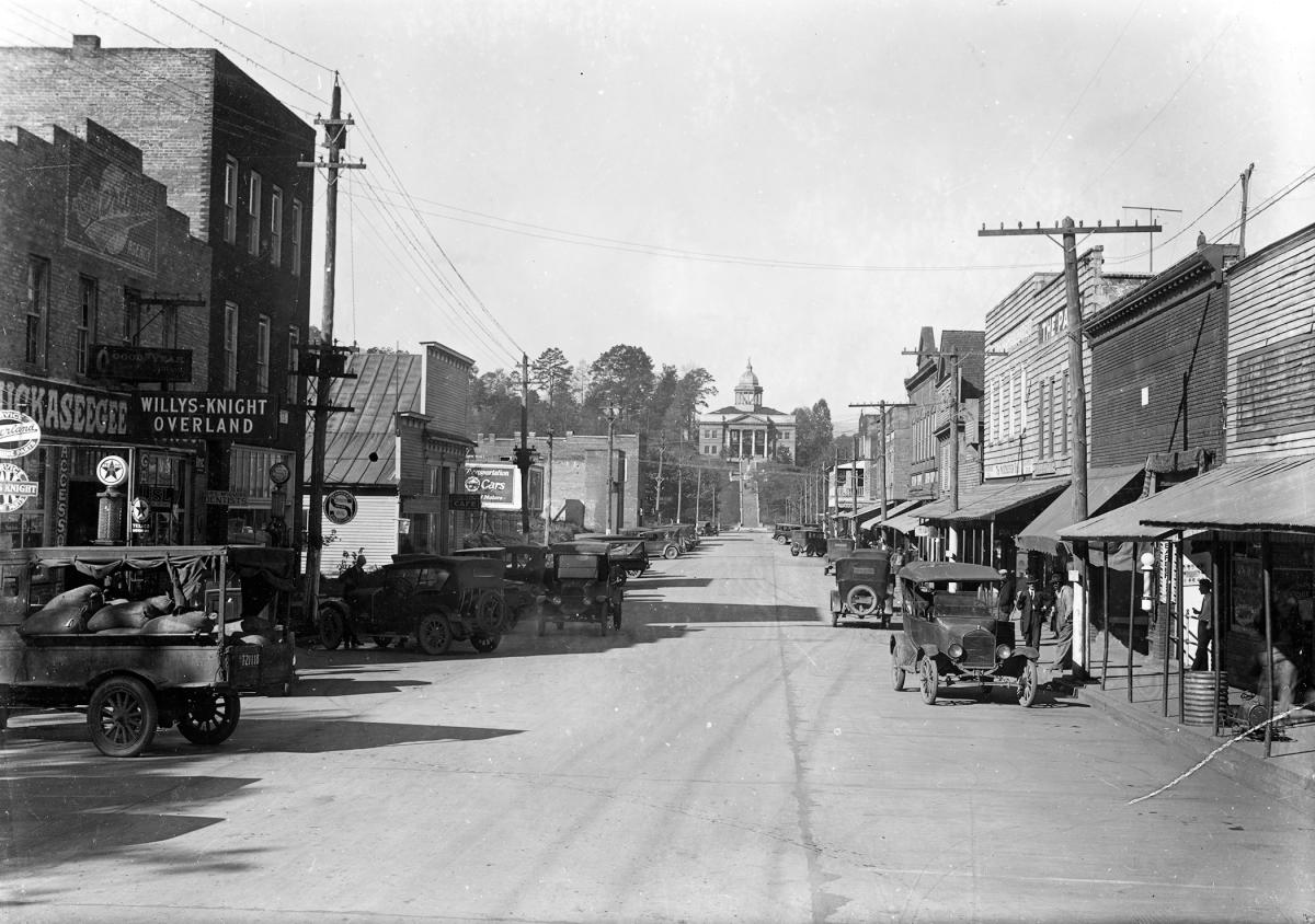 1920s view down unpaved Main Street in Sylva, NC, with Model T cars, a Willys-Knight Overland sign, The Paris and the courthouse on the hill ahead