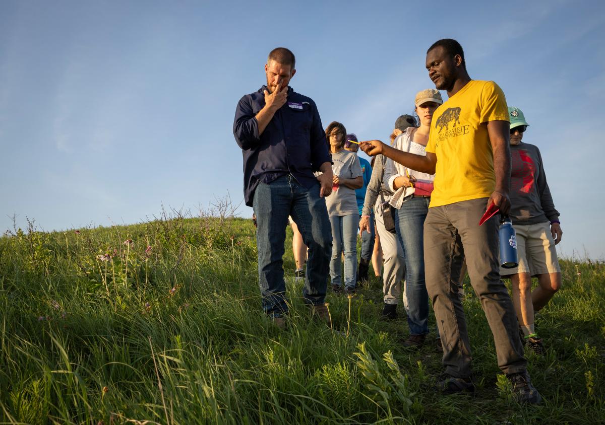 a group of people stand together looking at the native grass and wildflowers. A man in the front wears a yellow shirt with a bison on it.