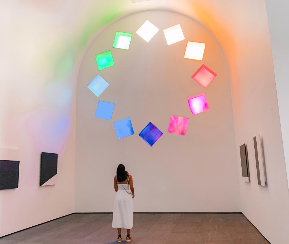 Woman in white jumpsuit admiring Kelly Eisworth's rainbow glass exhibit at the Blanton Museum.