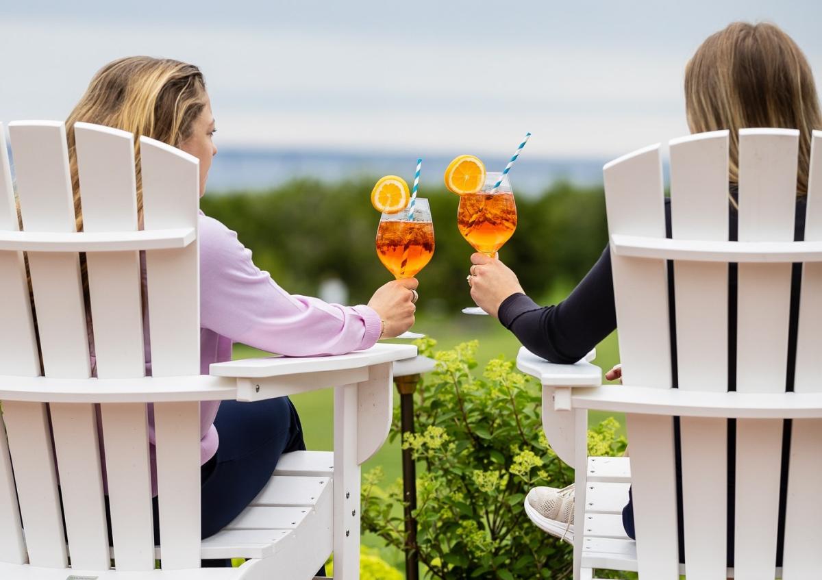 Two women sitting in Adirondack chairs relax with beverages at Mackinac Island’s Inn at Stonecliffe