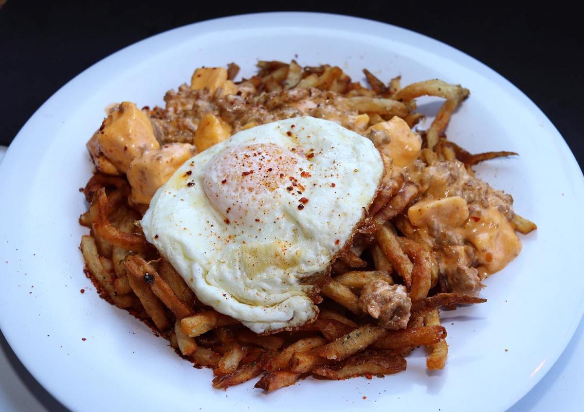 A hearty plate of crispy fries topped with melted cheese curds, savory gravy, and a perfectly fried egg sprinkled with seasoning.