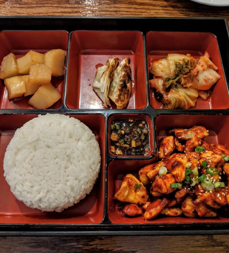 A red bento box with rice, dumplings, and other Korean dishes.