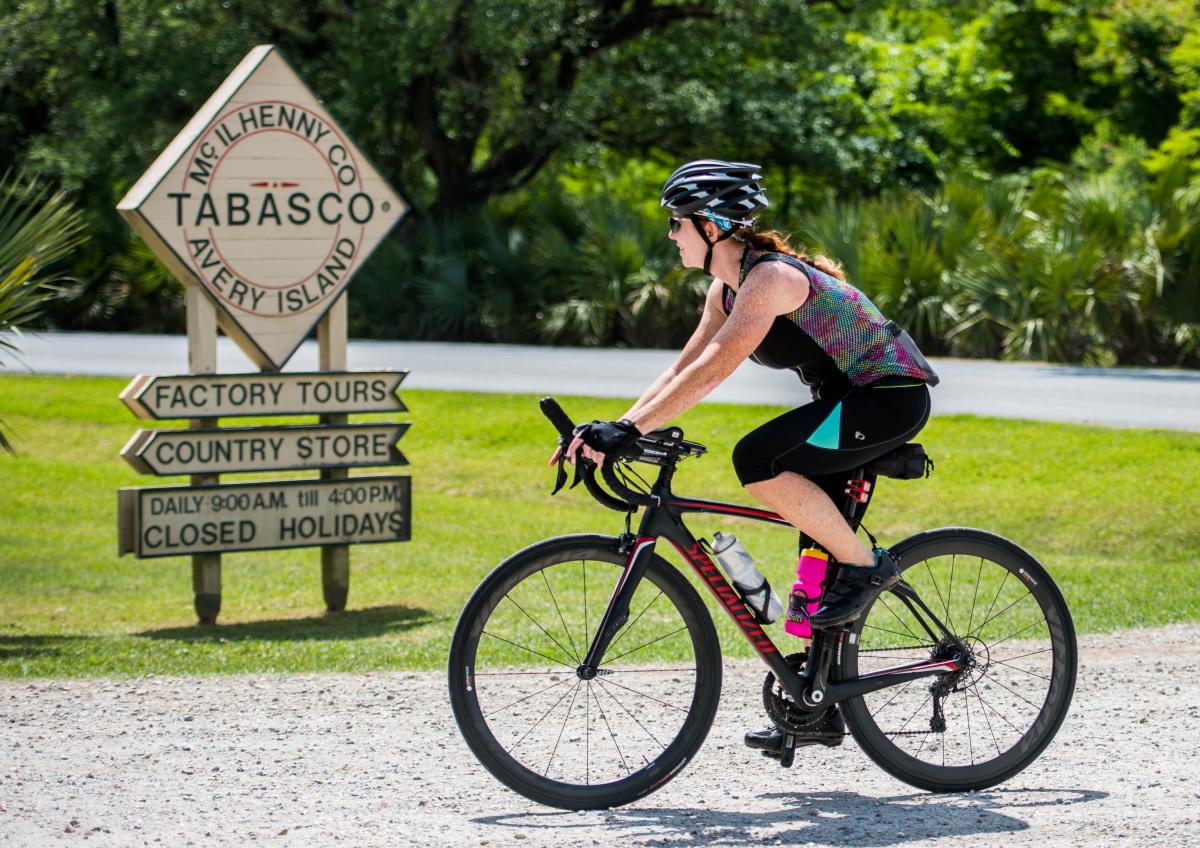 A woman passes the Tabasco factory sign on bike during Cycle Zydeco