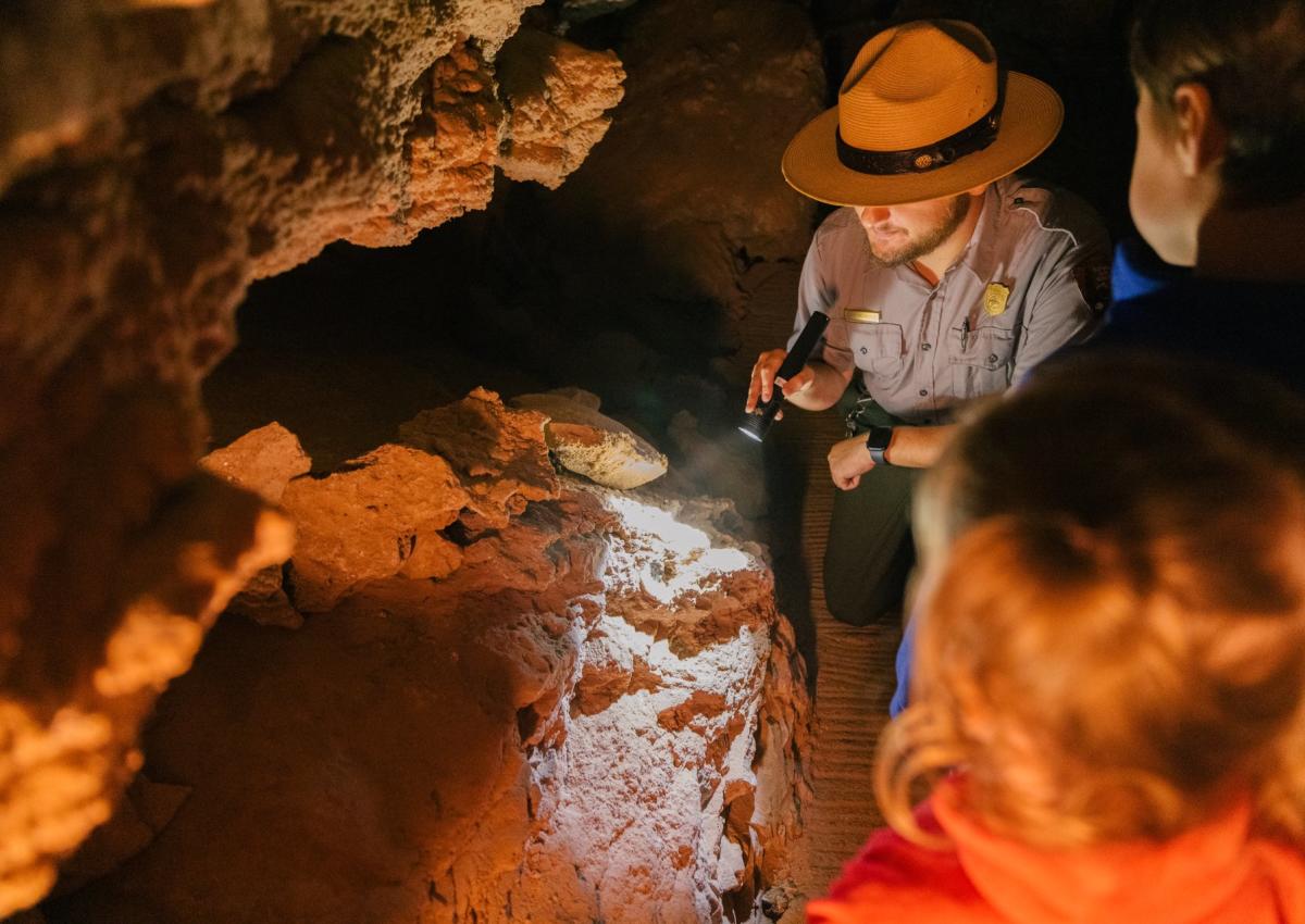 Wind cave park ranger on a guided tour with flashlight pointing at cave formation
