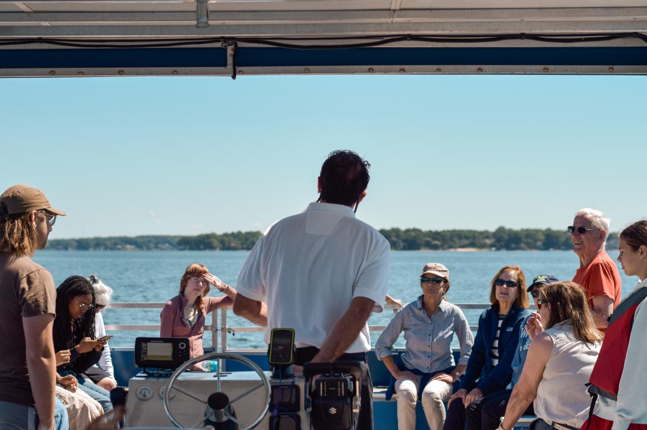 The captain is facing toward a group of people on the Catawba Riverkeeper Floating Classroom on Lake Norman.