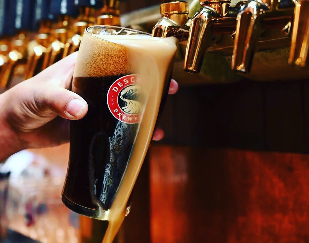 Image is of a dark beer being poured from the tap into the glass and the foam spilling over the glass.