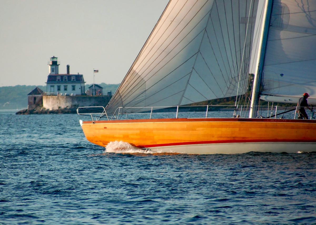 Yellow sailing 12 metre sailing boat on the water with Rose Island in the background.