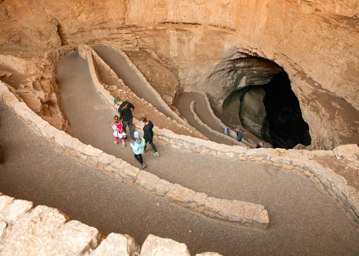 Visitors walking on a paved path inside Carlsbad Caverns National Park, approaching the entrance to the cave.