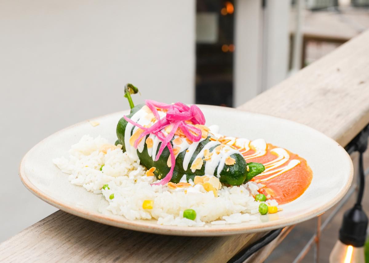 A plate with a poblano pepper dish on it sitting on a wooden railing outside of El Alma.
