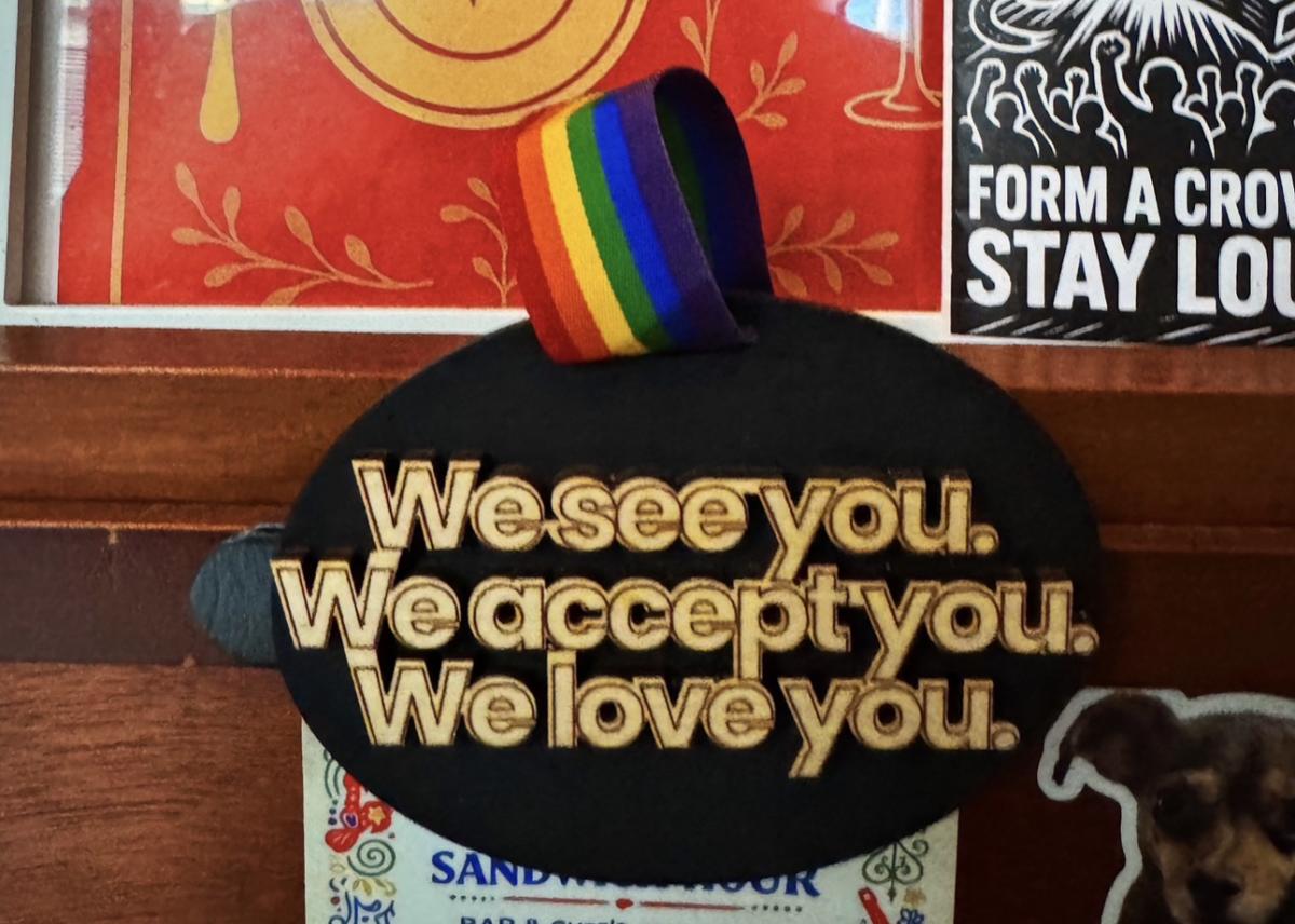 A rainbow-topped sign reads, “We see you. We accept you. We love you.”