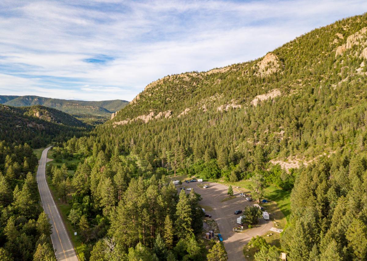 Aerial view of a scenic mountain landscape with a winding road and a parking area surrounded by dense forests.