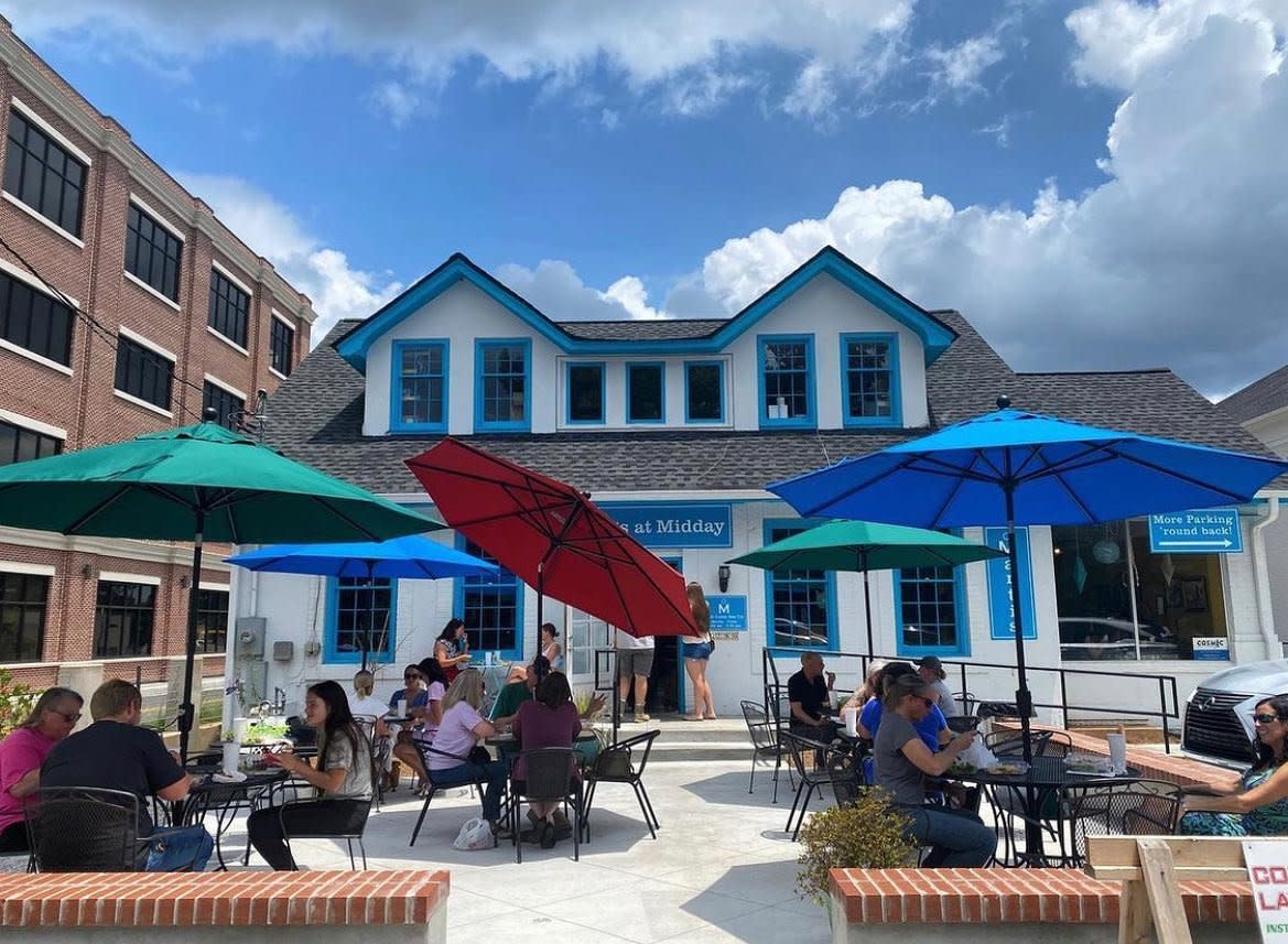 The patio at Marti's at Midday is shown. five tables, each with customers, are arranged on the cement patio. Each table has a colorful umbrella.