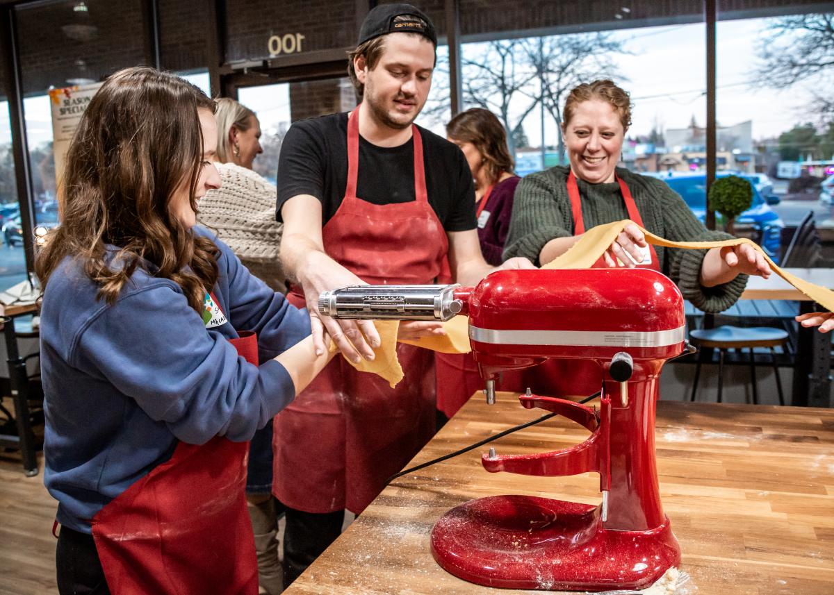 Three people standing around a mixer, making pasta.