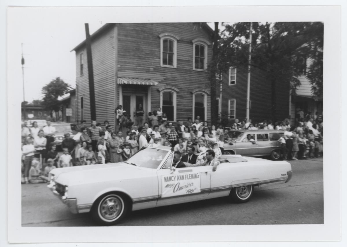 black and white photo of white convertible carrying Miss Michigan through a parade