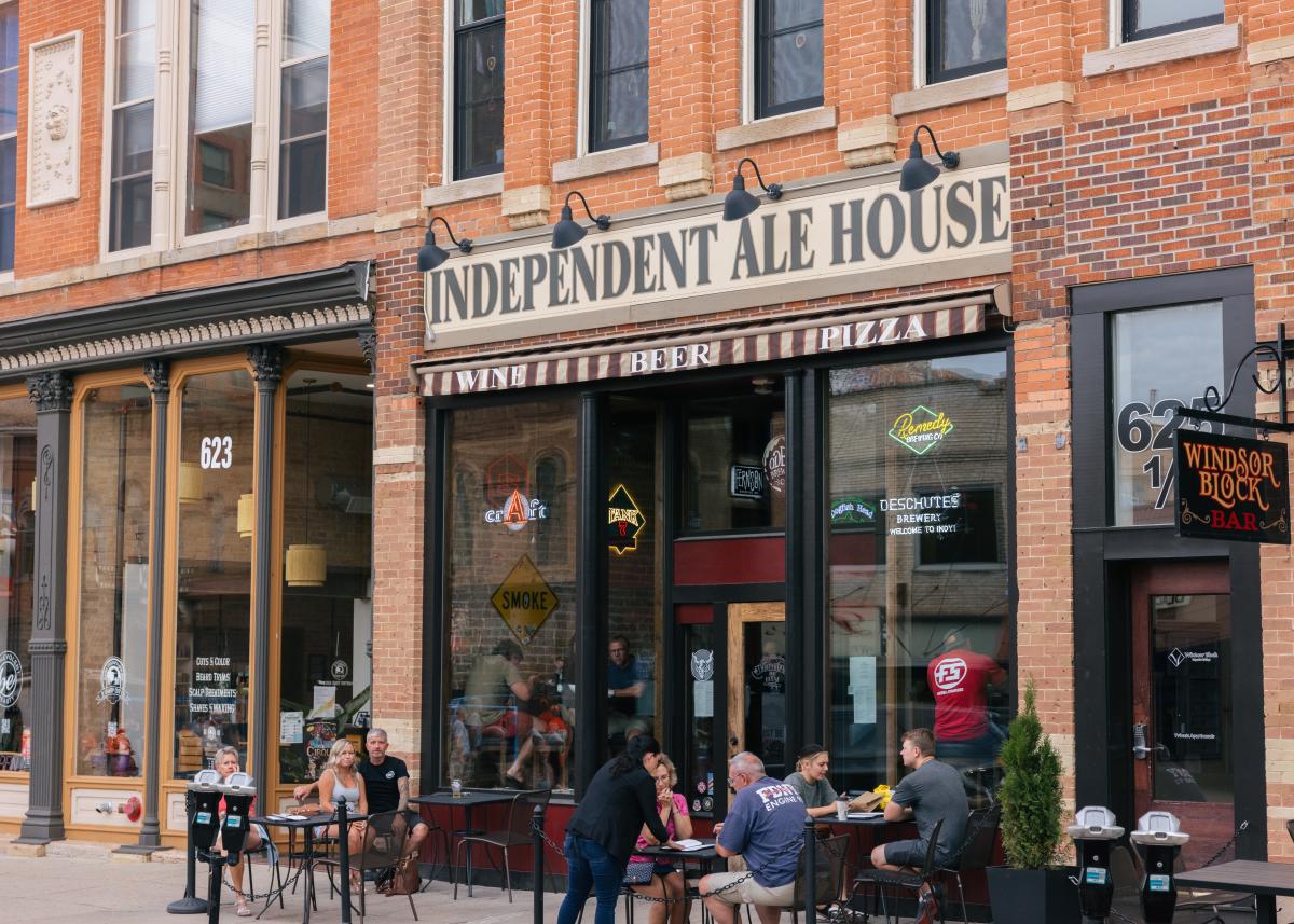 Street view of Independent Ale House, a brick building with large windows. Customers dine outside, creating a lively, friendly atmosphere.