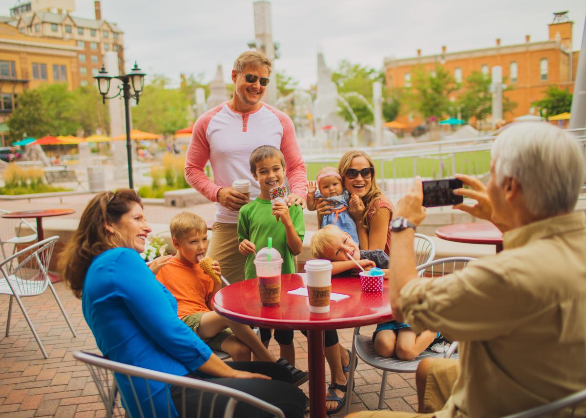 A group of smiling people, including adults and children, enjoy ice cream and drinks outside Silver Lining Creamery. One person takes a photo, capturing the joyful moment.