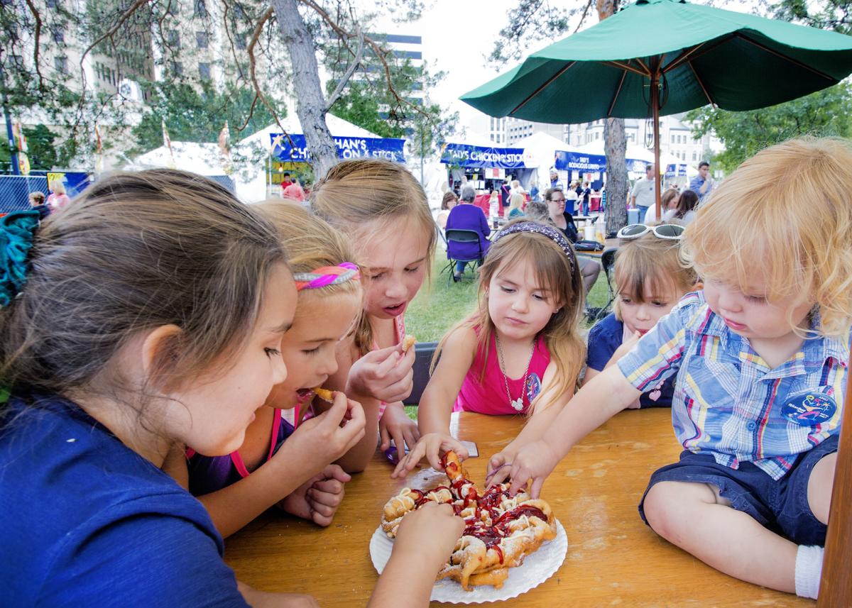 Six children eat a funnel cate at a table in the outdoor food court at Riverfest in Wichita.