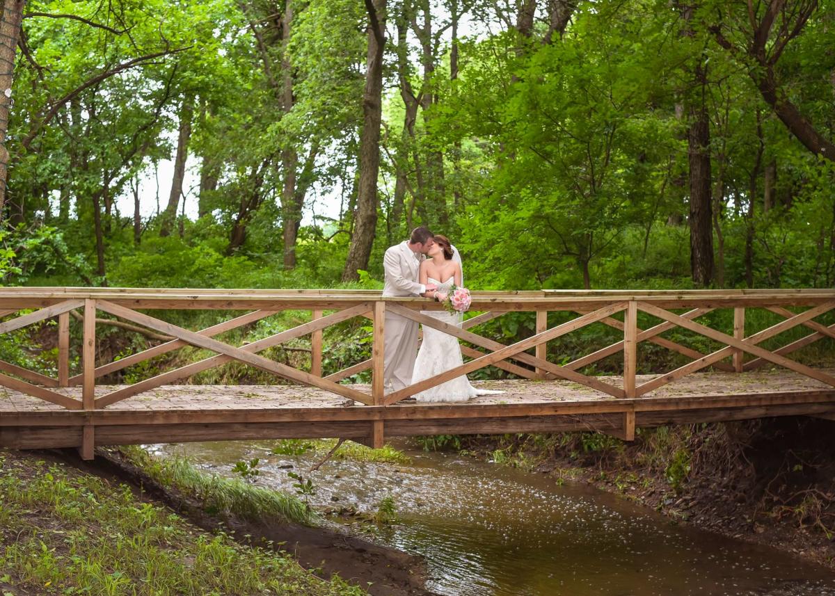 A bride and groom kiss while standing on a bridge over a creek at Fulton Valley Farms