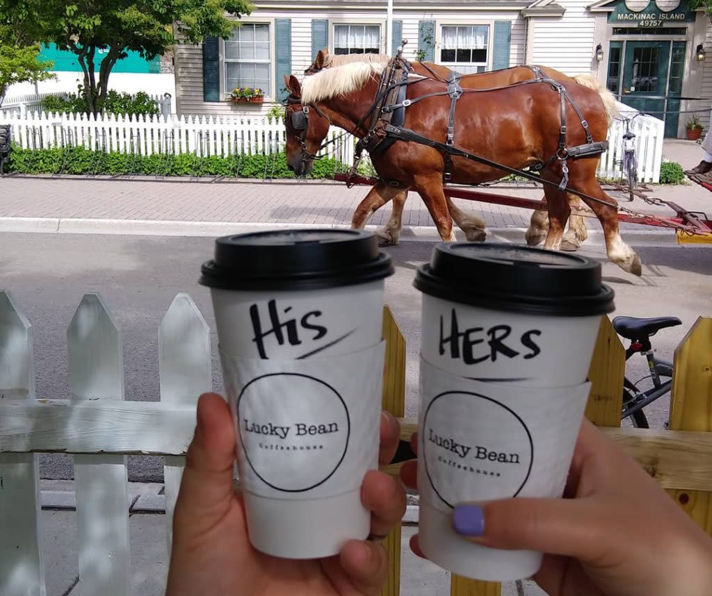 Couple Toasting with Cups of Coffee from Lucky Bean Coffee Shop in Front of Horse-Drawn Carriage on Mackinac Island