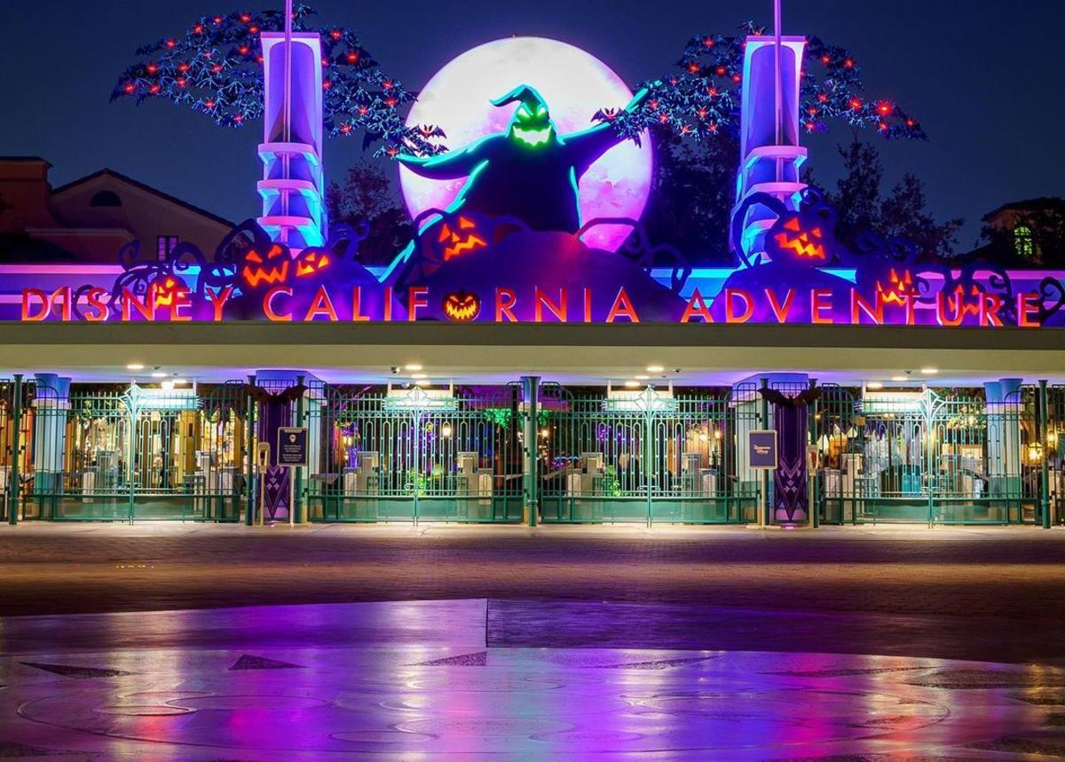Image of the front of Disney California Adventure Park. Image is taken at night and a sign reading 'Disney California Adventure' is lit up in red and purple lights. Oogie Boogie from The NightMare Before Christmas is seen above the sign.