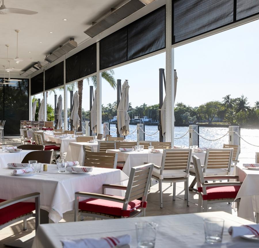 A covered waterside patio set for dining with white linens on the tables