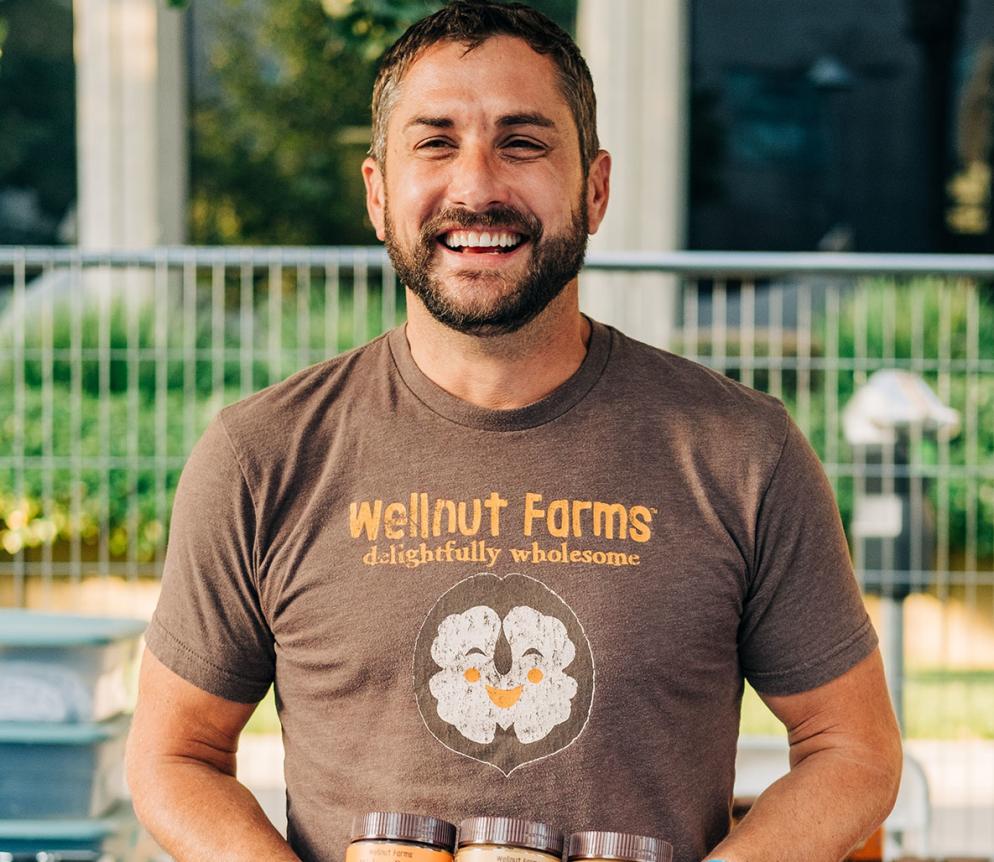 man holding small jars of nut butter with a shirt that says wellnut farms on it