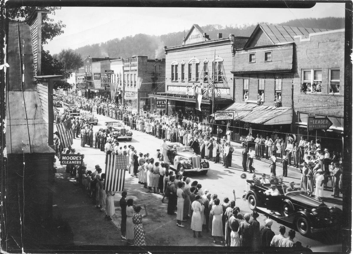 Crowds wave flags along Main Street in Sylva, NC, as President Franklin D. Roosevelt’s motorcade passes the C.J. Harris Building on Sept. 9, 1936