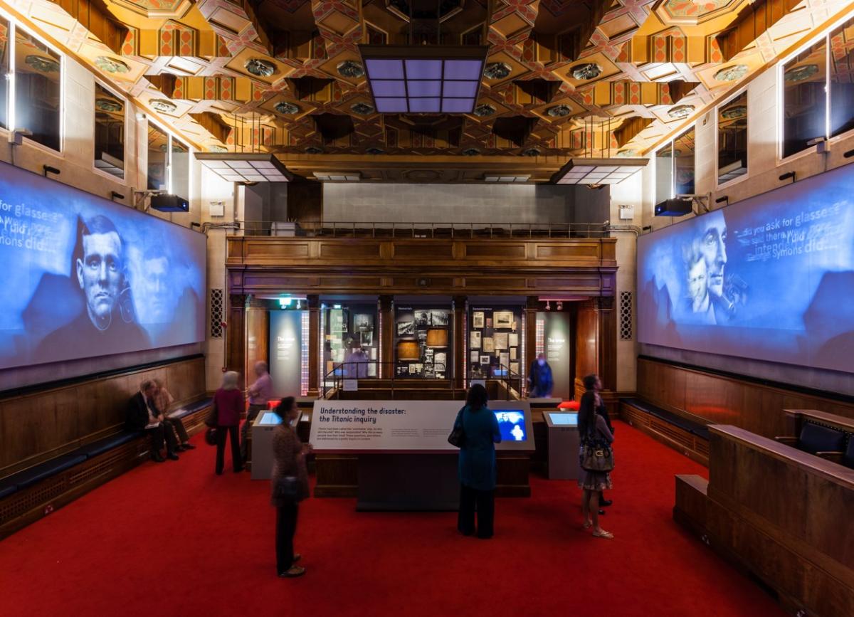 Inside the Titanic Exhibition at Seacity museum with people looking at information boards and screens on either side of the room