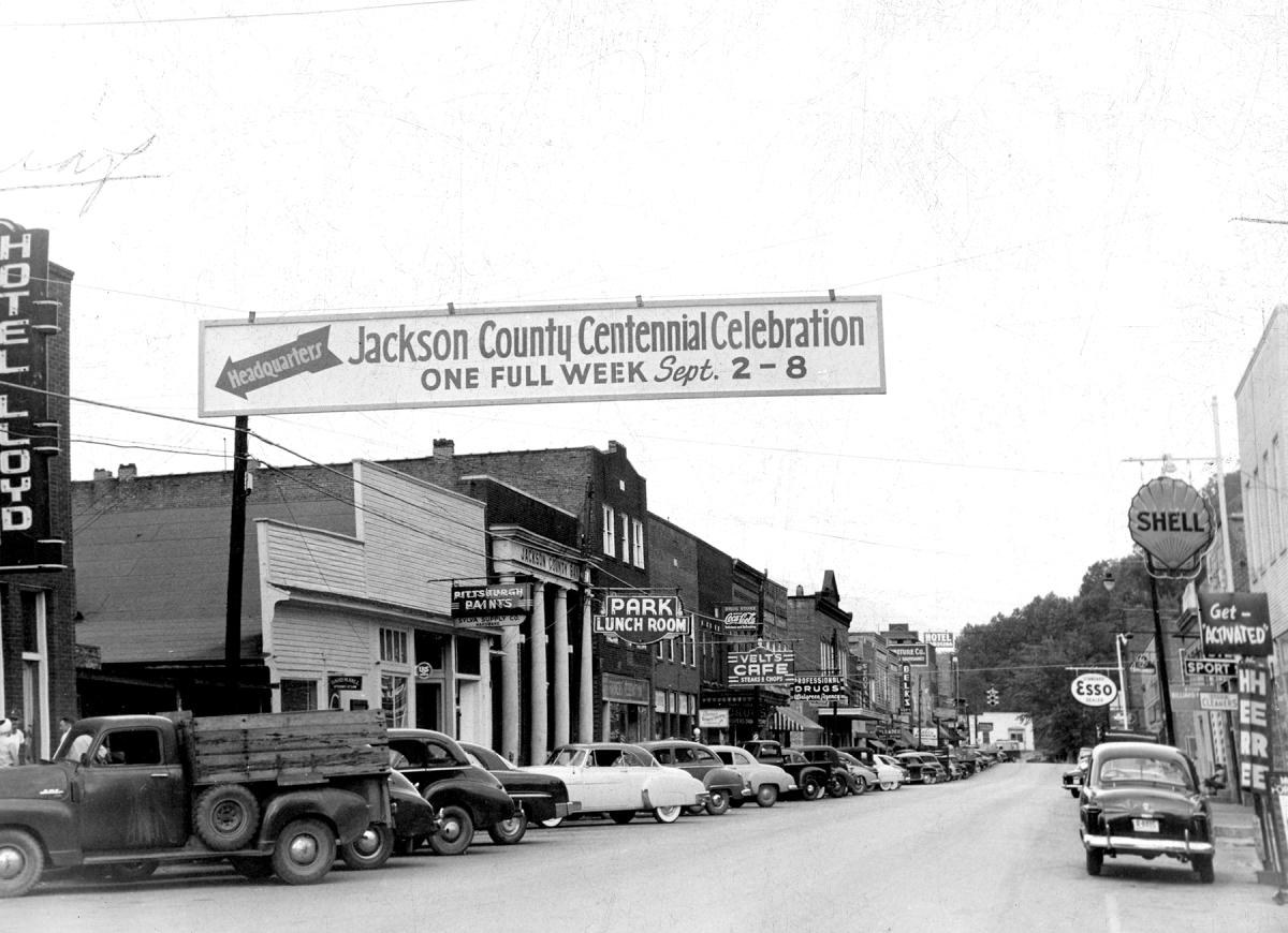 Banner for the Jackson County Centennial Celebration, Sept. 2-8, over Main Street in Sylva, NC, in 1951, with Hotel Lloyd, Velt’s Cafe and parked cars