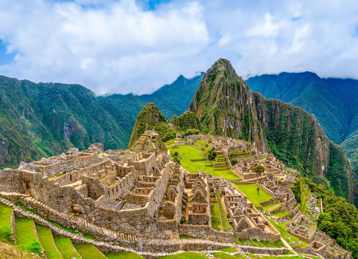 A panoramic view of Machu Picchu, a UNESCO World Heritage Site in Peru. The ancient Incan citadel is perched high in the Andes Mountains, surrounded by lush green terraces and dramatic mountain peaks.