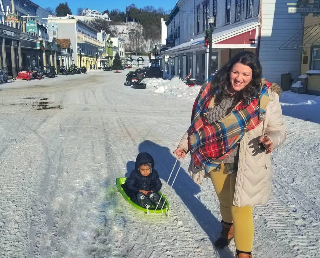 A woman pulls a little boy on a sled down a snow-covered Mackinac Island street during the holidays