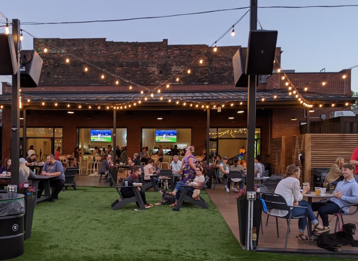 Strings of white lights hanging over Covington Yard, filled with seated people and a dog.