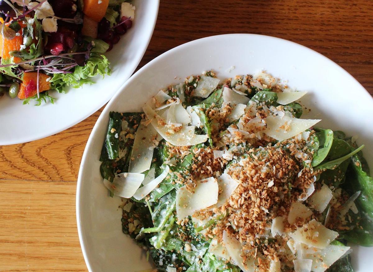 Image of a green Cesar salad in a white bowl with shaved parmesan cheese and breadcrumbs.