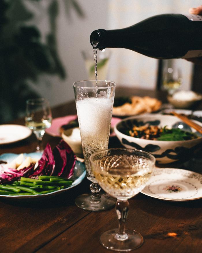 A table set with various dishes with a focus on bottle pouring champagne into a glass