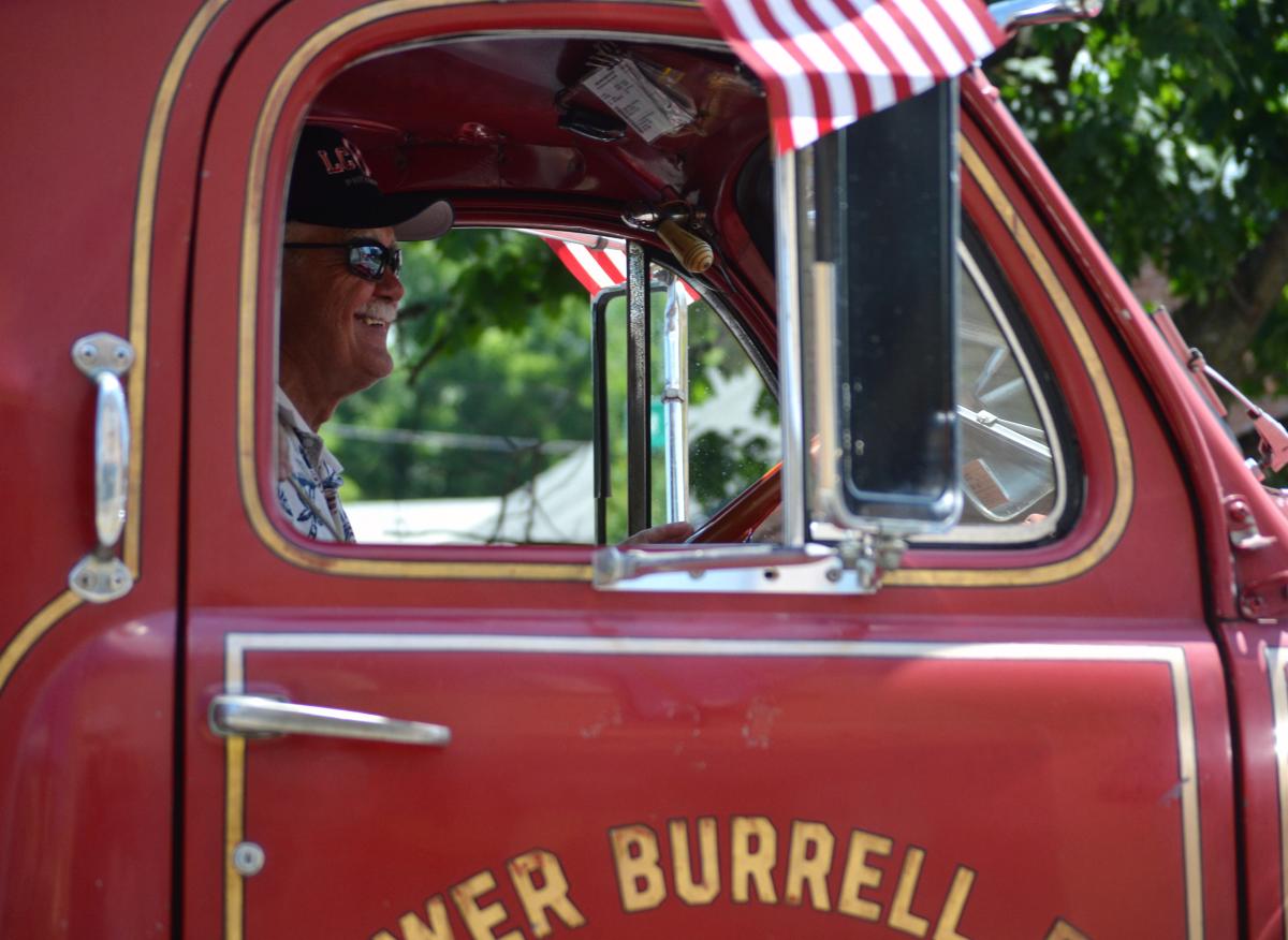 Smiling driver of a vintage red fire truck with an American flag during a Fourth of July parade in Loudoun County