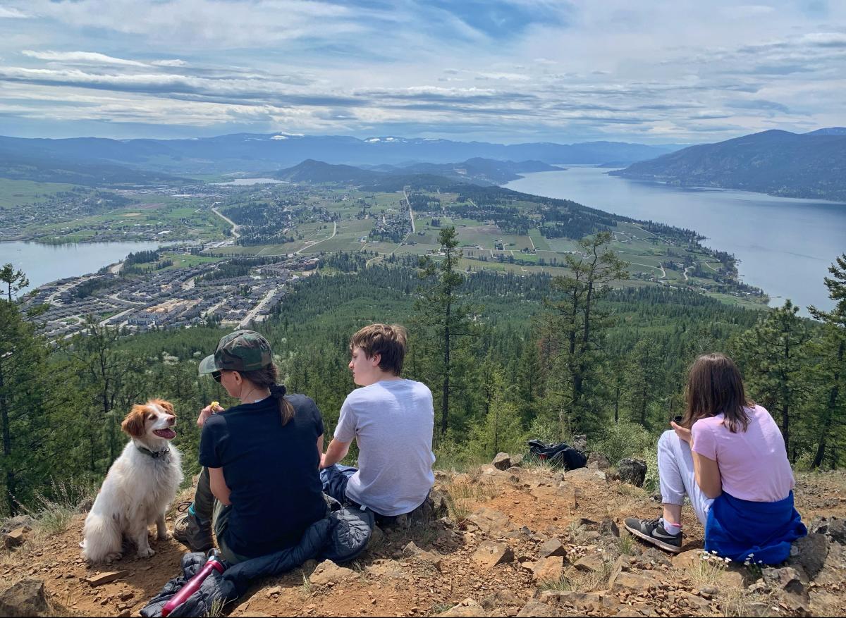 A mother with teenage boy and girl sit on a mountainside overlooking Kelowna with their dog Credit Lisa Kadane - Spion Kop