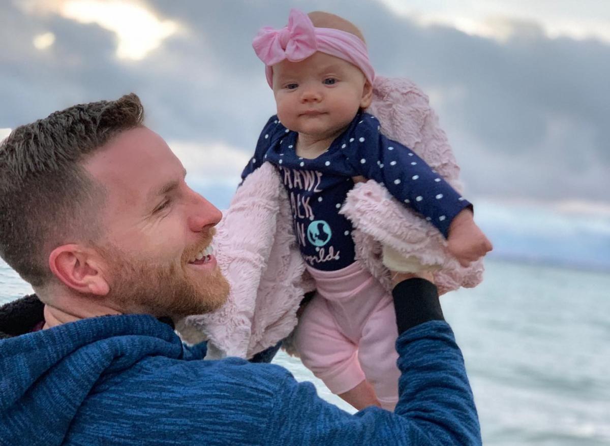 A man holds up a baby near the water on Mackinac Island